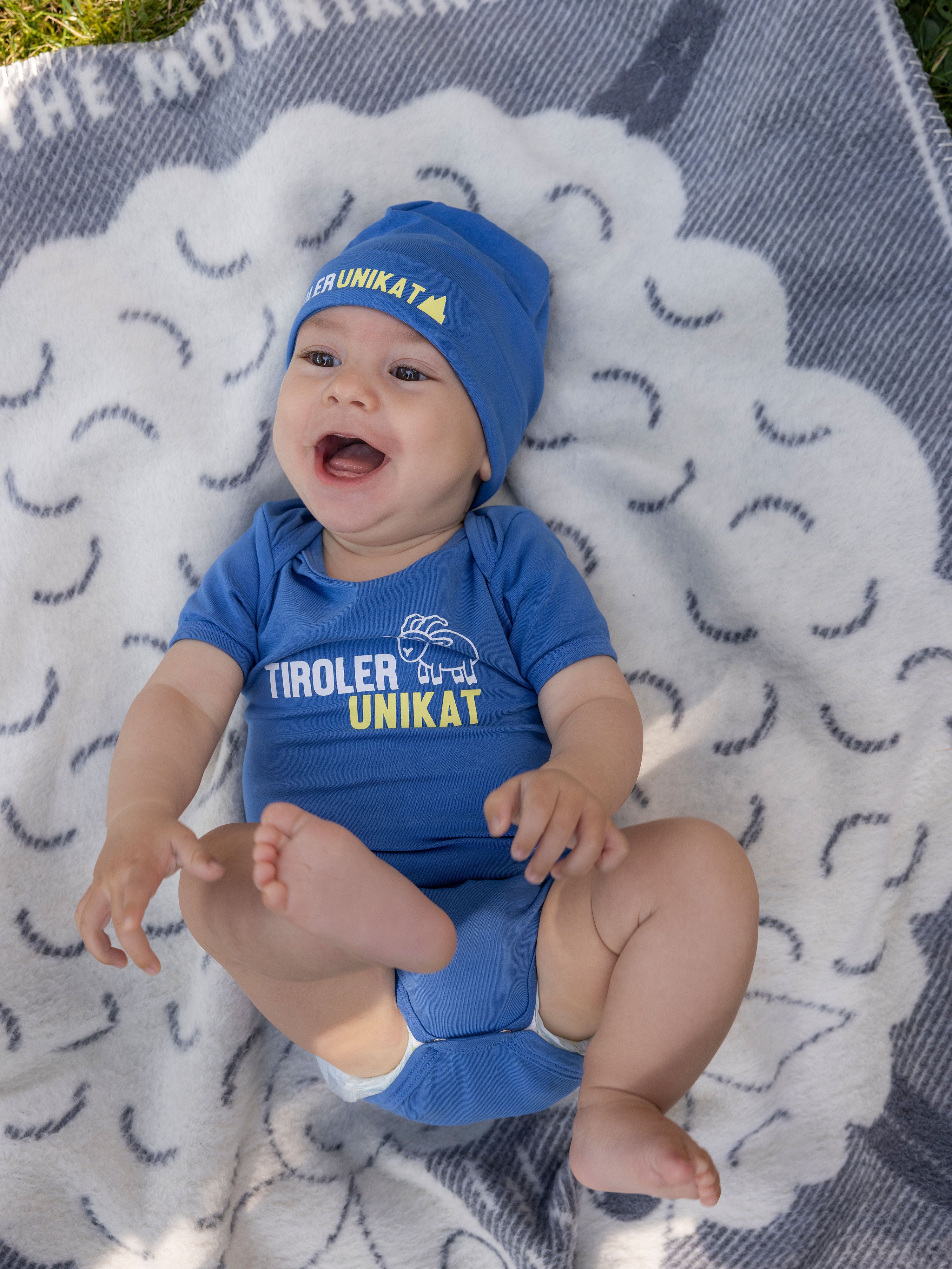 Das Set Baby Body und Beanie "Tiroler Unikat" wird von einem Baby getragen.