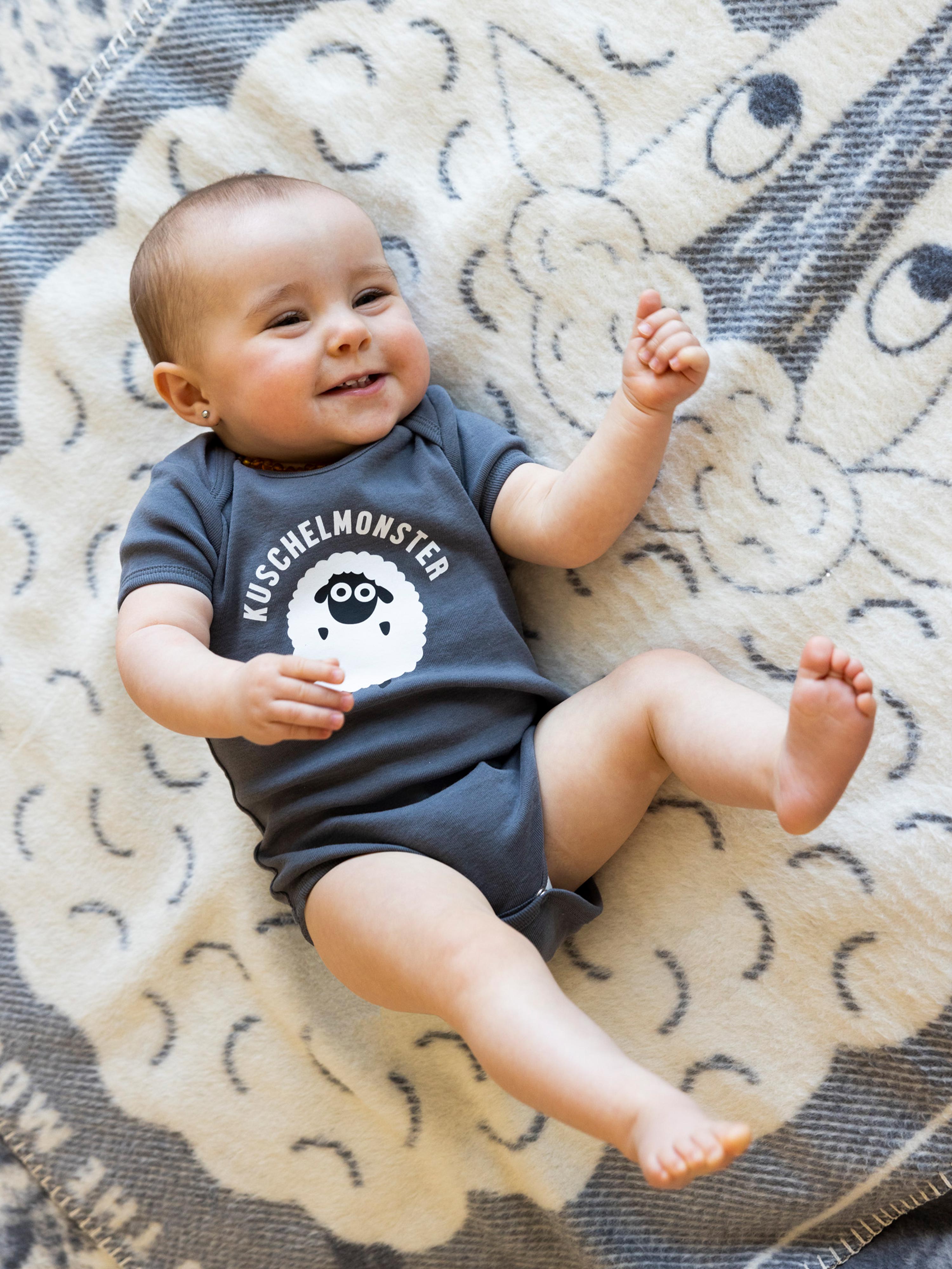 Baby mit Baby Body in Anthrazit und süßem Schaf-Print auf der Brust.