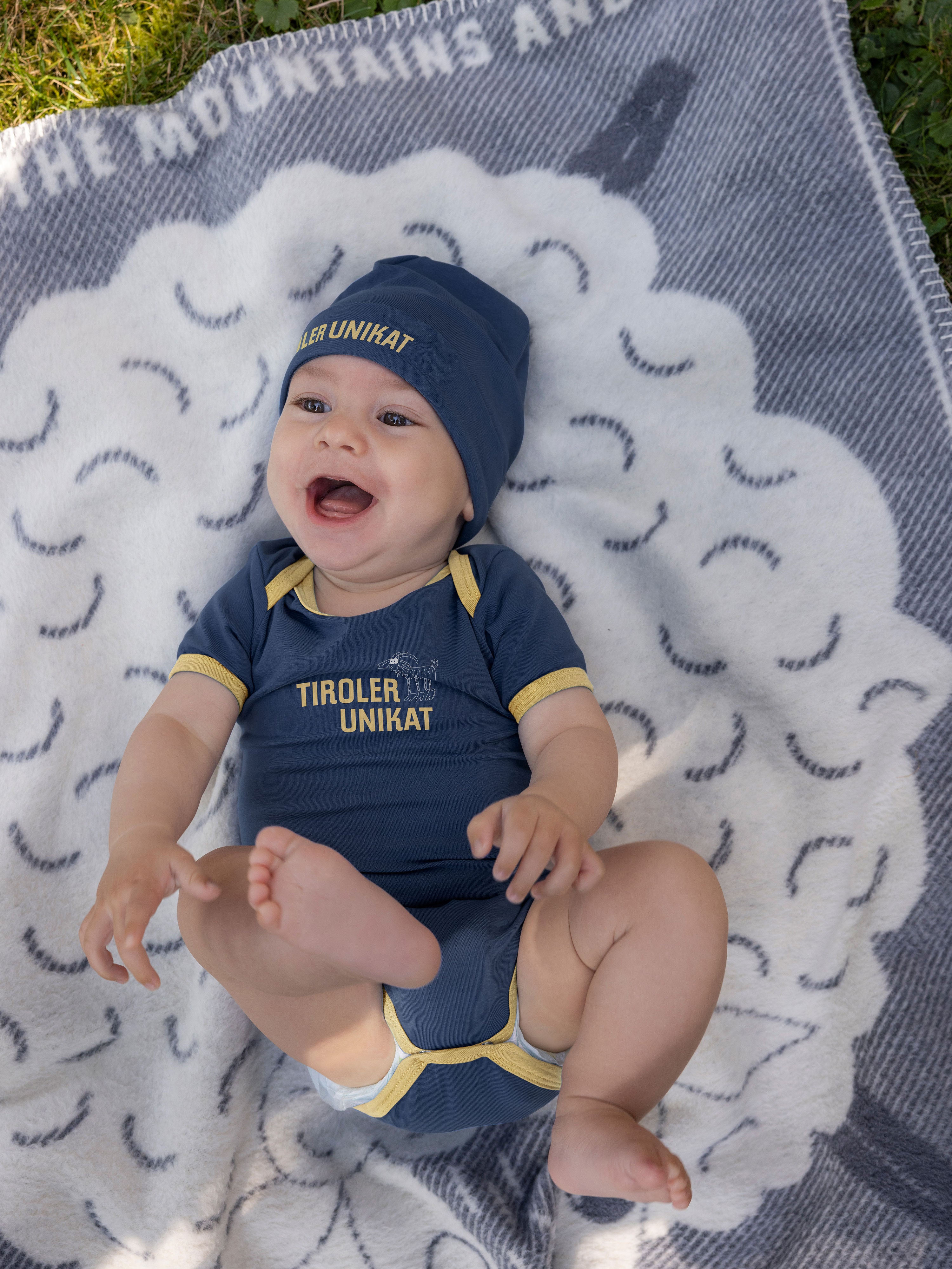Baby trägt Baby Body und Beanie mit Tiroler Unikat Aufdruck