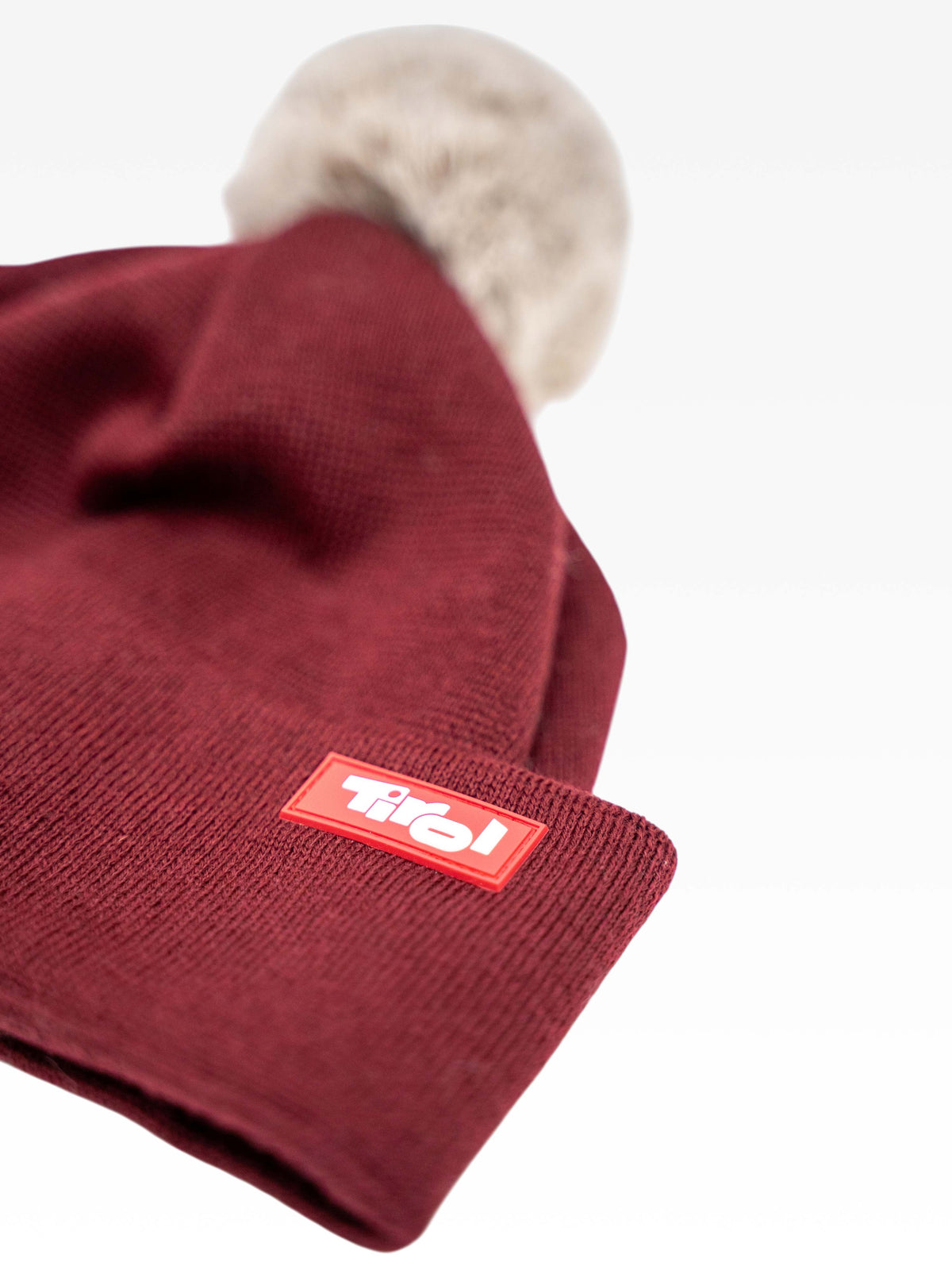 Strickmütze "Tanja" in Dunkelrot mit beigem Bommel und Tirol Logo auf der Stulpe