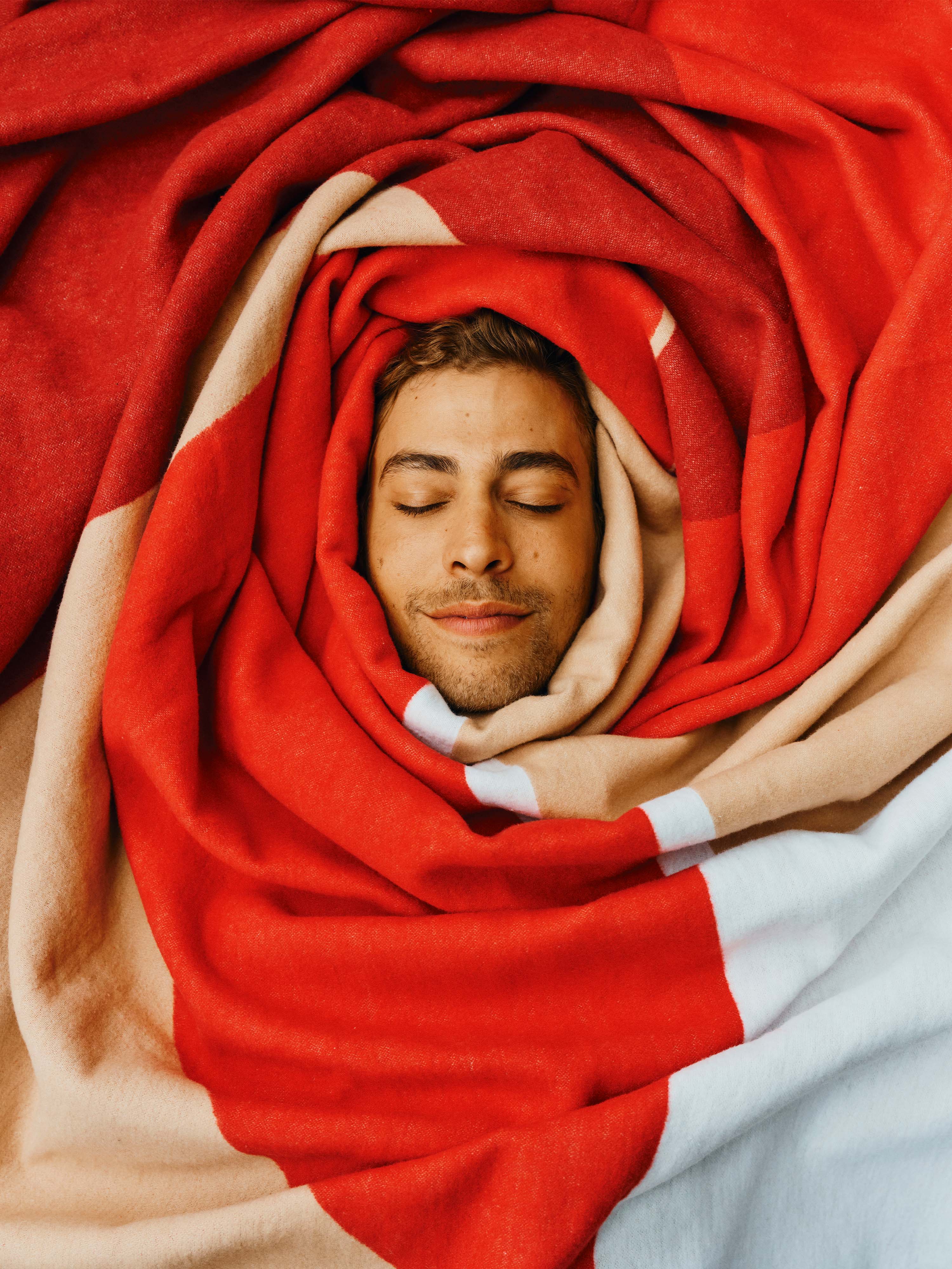 Der Kopf von einem Mann ist in die rote Decke "Georg" eingekuschelt.