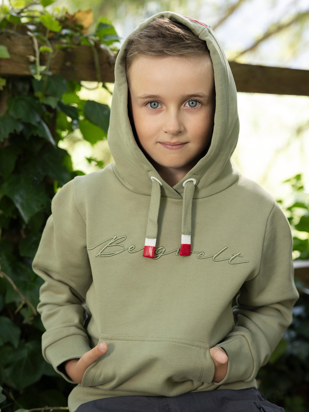 Ein Bub trägt den Kinder Hoodie "Bergwelt" in Zementgrau mit Kapuze