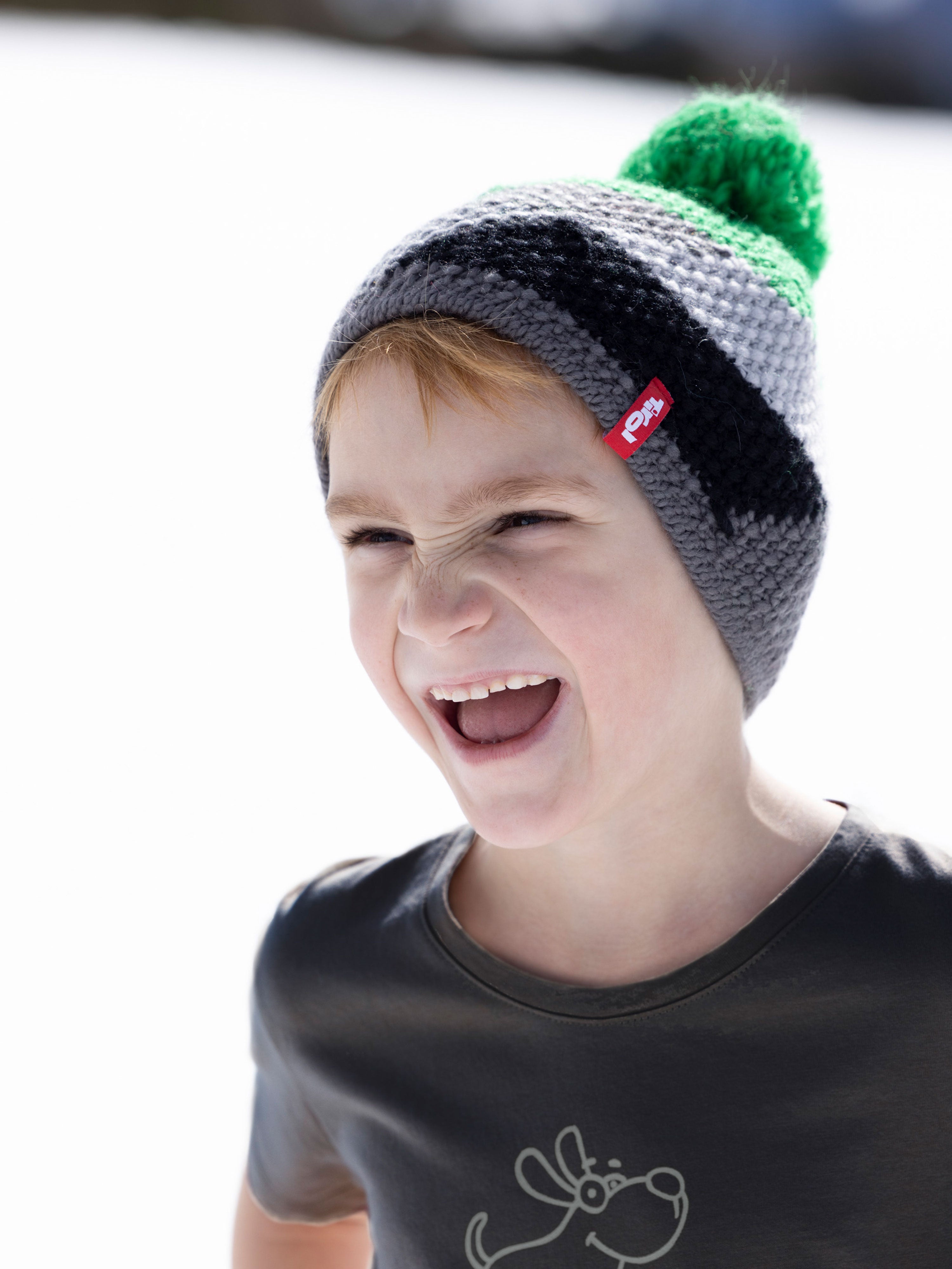 Ein fröhlicher Bub trägt die Kindermütze "Florian" aus dem Moments Tirol Shop.