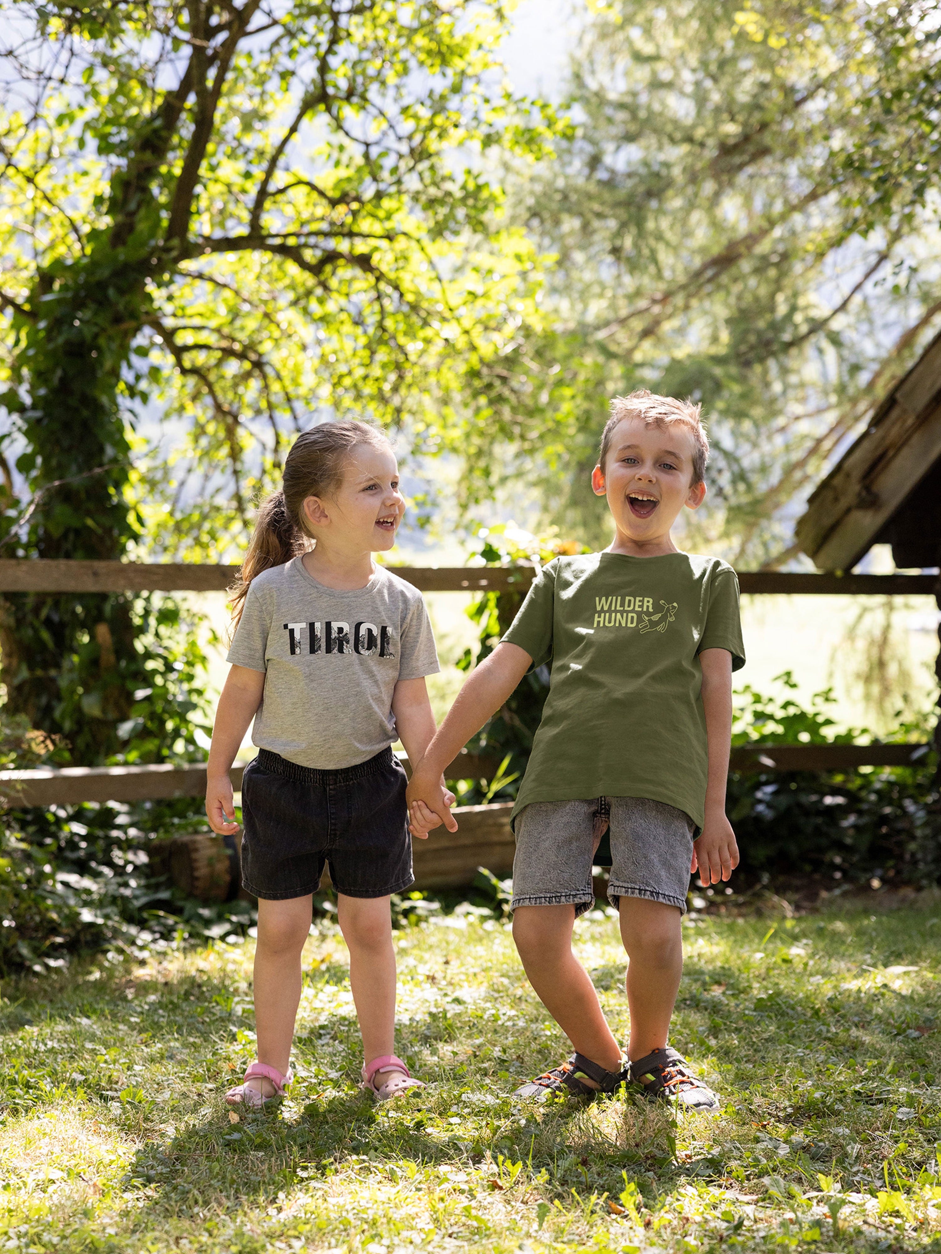 Mädchen und Junge stehen freudig im Gras mit t Shirt aus Bio Baumwolle 