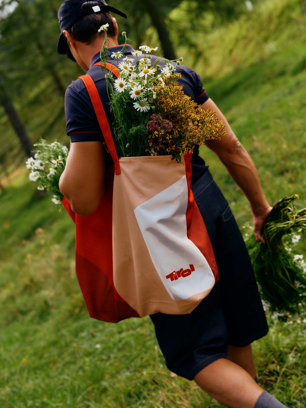 Ein Mann trägt die neue Strandtasche "Elenora" im neuem Tirol- Design in Rot mit Blumen gefüllt