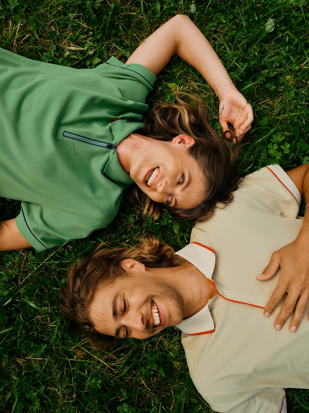 Ein Mann und eine Frau liegen im Gras und tragen das Polo Shirt "Noah" in Grün und das Polo Shirt "Peter-Paul" in Beige.