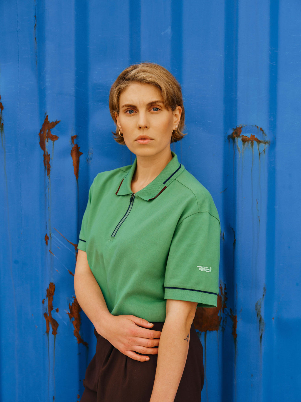 Eine Dame steht vor einem blauen Hintergrund und trägt das Unisex Polo Shirt "Noah" in Grün.