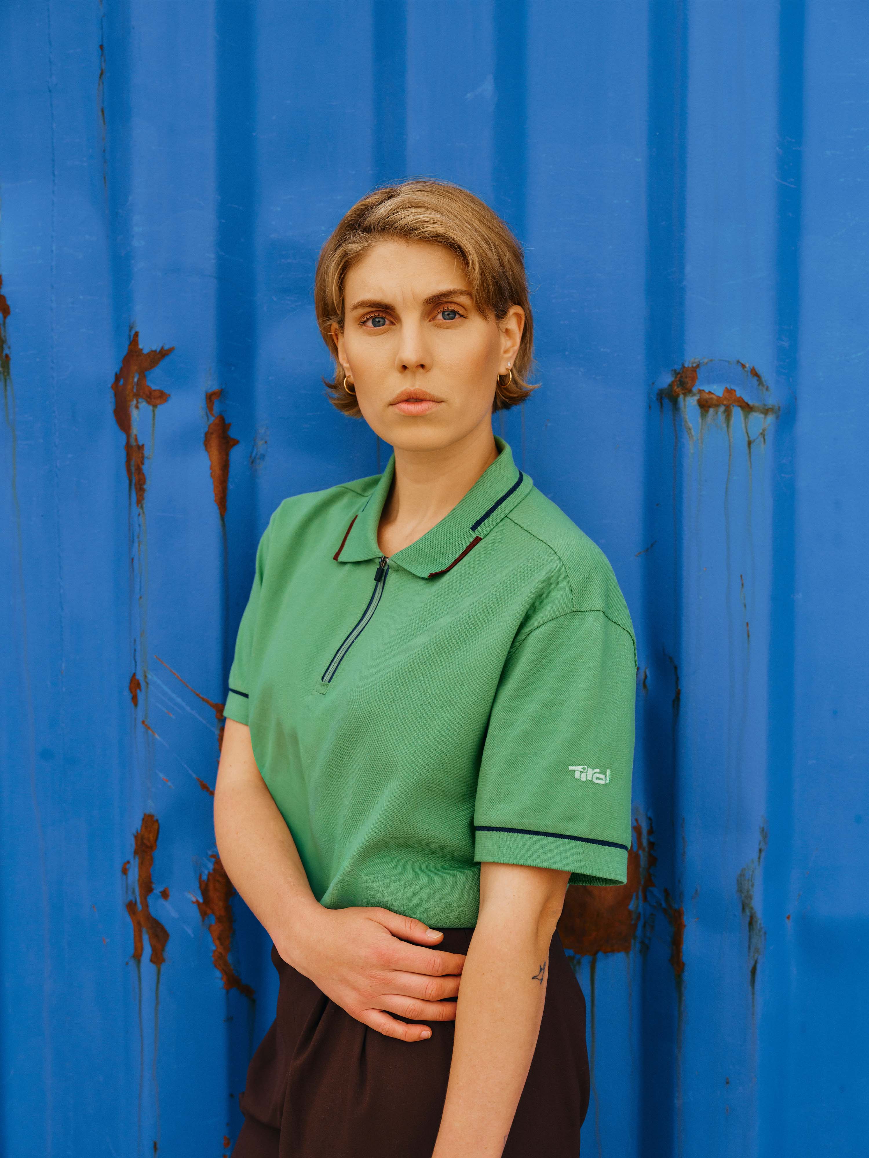 Eine Dame steht vor einem blauen Hintergrund und trägt das Unisex Polo Shirt "Noah" in Grün.