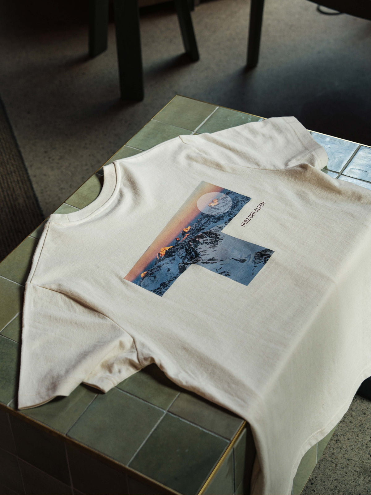 Das Unisex T-Shirt "Wildspitzbahn" in Natur liegt auf einem grünen Fließenblock.