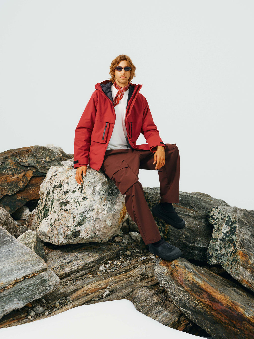 Ein Mann sitzt auf einem Felsen und trägt die Unisex Winterjacke "Toni" in Rot offen