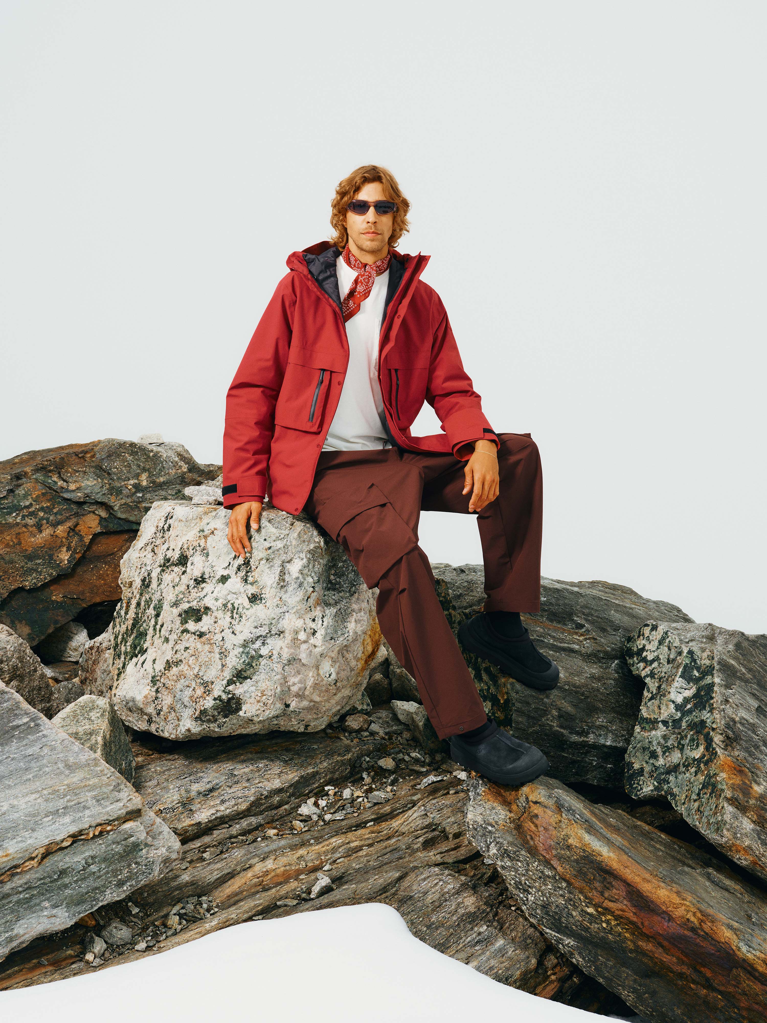Ein Mann sitzt auf einem Felsen und trägt die Unisex Winterjacke "Toni" in Rot offen